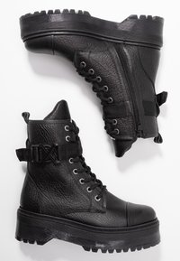 Stivali alla caviglia in pelle nera con finitura testurizzata, design con lacci, zip laterale, cinturino regolabile e suole spesse e rigate.