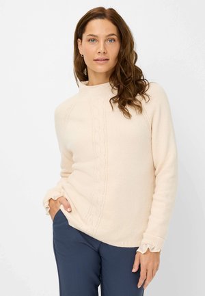 Maglioncino crema a maglia con motivo a trecce e collo alto; presenta polsini a costine e una vestibilità rilassata. Abbinato a pantaloni blu navy.