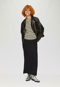 Schwarze Lederbikerjacke über einem beigen und schwarzen gestreiften Hemd, kombiniert mit einem schwarzen Maxirock und silbernen metallischen Knöchelstiefeln.