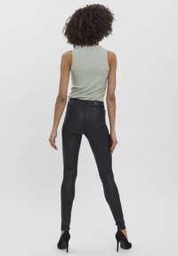 Pantalons ajustés en simili cuir noir avec poches arrière, associés à un haut sans manches en ribbed vert clair. Le mannequin porte des talons noirs.