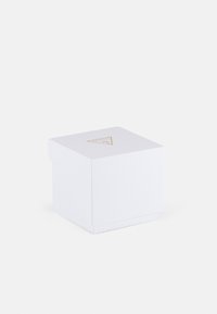 Hvit firkantet boks med teksturert finish, og et gullfarget logo i en trekant på lokket. Rent design med en minimalistisk estetikk.