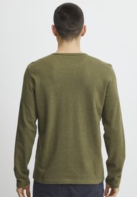 Long-sleeve, olive green shirt made of textured fabric, featuring a rounded neckline and cuffs, with a straight hem at the waist.
