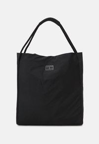 Svart axelväska i texturerad tyg med två långa handtag och en liten logopatch på framsidan. Rymlig design med minimalistisk stil.