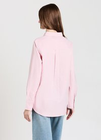 Light pink long-sleeve shirt with a collared neck, button cuffs, back pleat, and a rounded hem, made of soft, textured fabric.