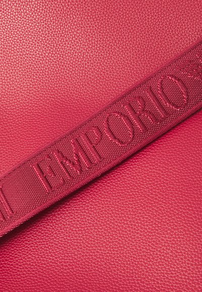 Raudona tekstūruota oda su reljefine "EMPORIO" etikete. Dizainas turi lygų paviršių ir drąsią, pintą diržo detalę.