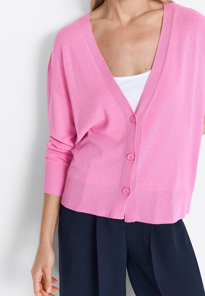 Cardigan rose clair avec un décolleté en V profond, cinq boutons à l'avant et des poignets et un ourlet côtelés. Fabriqué en tissu tricoté doux, offrant une coupe décontractée.