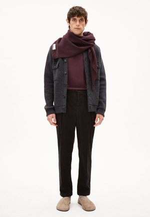 Dunkelgraue Wollstrickjacke über einem kastanienbraunen Langarmshirt, kombiniert mit schwarzen Hosen und beigen Slippern. Ein weinroter Schal ist um den Hals gewickelt.