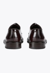 Scarpe in pelle marrone con finitura lucida, punta arrotondata e tacco incassato. Dettagli di cucitura minimi esaltano il design complessivo.