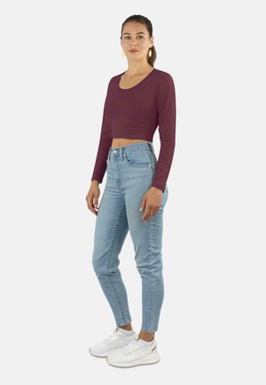 Burgundy long-sleeve crop top paired with light blue high-waisted jeans. The outfit is complemented by white athletic shoes.