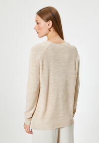 Beige randig stickad tröja med långa ärmar, rundad hals och en lätt avslappnad passform; har en mjuk textur och subtila färgvariationer.