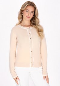 Cardigan beige chiaro con scollo rotondo, chiusura frontale con bottoni e dettagli bianchi lungo la patta e i polsini. Texture a maglia morbida.
