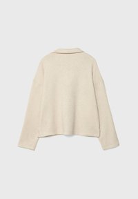 Maglione beige a manica corta con una consistenza morbida. Presenta un colletto, spalle scese e spacchi laterali all'orlo per facilitare i movimenti.