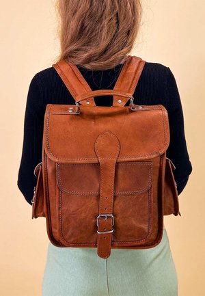 Sac à dos en cuir marron avec bretelles ajustables, rabat avant et fermeture à boucle. Doté d'une texture lisse et de détails de couture.