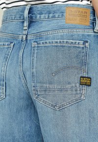 Modré denimové džíny s vybledlým vzhledem, vybavené dvěma zadními kapsami a štítkem G-Star Originals na pásku.