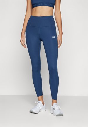 Marineblå strækleggings med høj talje og et synligt New Balance-logo på venstre lår, lavet af glat, tætsiddende stof.