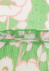 Bloemenstof in groen en wit met roze accenten. Doorzichtige textuur met een gerimpelde zoom en zichtbare plooien die verticaal lopen.