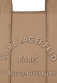 Beżowa skórzana torba tote z wytłoczonym tekstem: "Karl Lagerfeld Paris" oraz "21 Rue St-Guillaume", z delikatnymi detalami przeszycia.