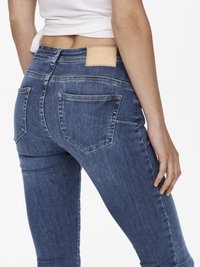 Jeans de ganga azul skinny com uma cintura alta, apresentando um patch de couro na parte de trás, dois bolsos traseiros e desbotamento subtil.