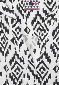 Tissu à motifs noir et blanc avec des diamants et des zigzags. Design en V avec une étiquette indiquant "Hola Mi Sol". Matériau en coton texturé.