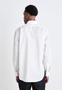 Weißes Hemd mit klassischem Kragen, langen Ärmeln und abgerundetem Saum. Glattes Baumwollmaterial mit minimaler Detailbeschreibung.