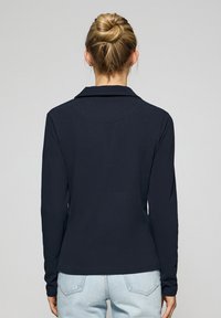 Camisa de manga larga azul marino con cuello, con una textura suave y un corte recto en el dobladillo. Detalles de costura visibles en las costuras.