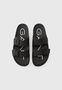 Black sandals made of durable material with two adjustable straps, featuring a buckle design, and a white logo on the footbed.