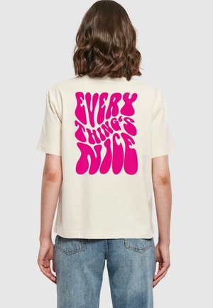 T-shirt di cotone color crema con maniche corte. Presenta un bold testo rosa testurizzato sul retro che recita "TUTTO È BELLO."