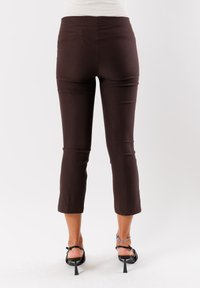 Pantaloni cropped marroni realizzati in un tessuto elasticizzato, con un design aderente e una vita. L'orlo termina appena sopra la caviglia.