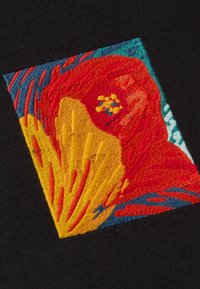 Parche bordado con vibrantes colores rojo, naranja, amarillo y azul sobre un fondo de tela negra, que representa formas y texturas abstractas.
