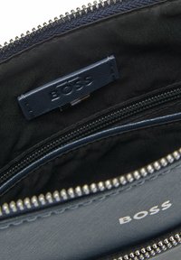 Wnętrze granatowego skórzanego portfela z zamykanymi na zamek przegródkami, charakteryzujące się gładką fakturą oraz skórzaną metką z wytłoczonym napisem "BOSS".