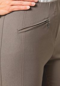 Grijze rekbare broek heeft een snug fit met een ritszak aan de zijkant en zichtbare stiksels langs de naden.