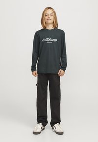 Ciemnozielona koszula z długim rękawem z białym logo "Jack & Jones", w połączeniu z czarnymi spodniami cargo z bocznymi kieszeniami i białymi trampkami.
