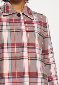 Kariertem Mantel mit einem Farbschema in Pink, Rot, Braun und Blau, mit Kragen und Einzelknopfverschluss; aus strukturiertem Stoff gefertigt.