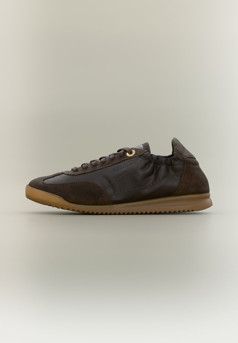 Baskets décontractées marron foncé avec panneaux en daim et cuir, lacets, arrière élastique, et semelle en caoutchouc naturel sur un fond neutre.