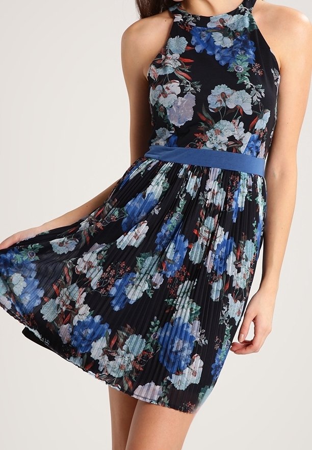 Robe à col licou florale avec un fond noir, des motifs floraux bleus et blancs, une jupe plissée et une ceinture bleue pour accentuer.