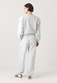 Szara bluza i dopasowane spodnie dresowe wykonane z miękkiego materiału, charakteryzujące się luźnym krojem i ściągaczami. Wyświetlane od tyłu.