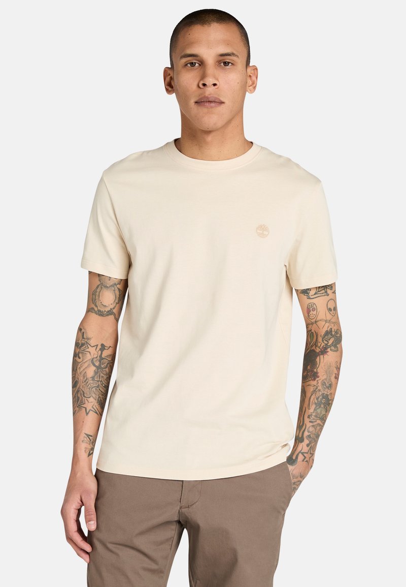 Béžové bavlněné tričko s kulatým výstřihem a krátkými rukávy; na hrudi má malé tónované logo. Hladká textura a přiléhavý střih.