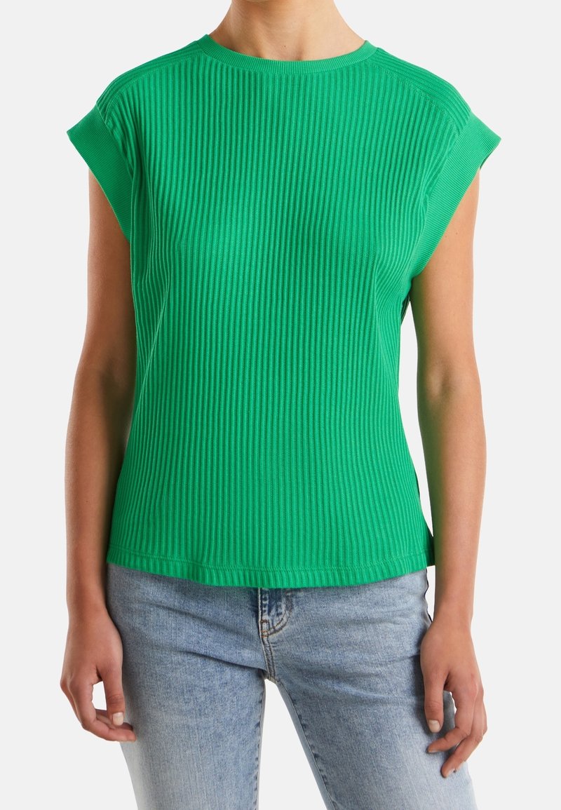 Zelený pletencový top s krátkým rukávem a kulatým výstřihem a ohrnutými rukávy. Látka je texturovaná a vytváří vertikální pruhy. V kombinaci s světle modrými džíny.