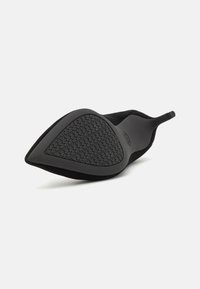 Scarpa nera a punta con suola in gomma texturizzata, tomaia in tessuto elegante e un design minimalista con un anello al tallone per indossarla facilmente.