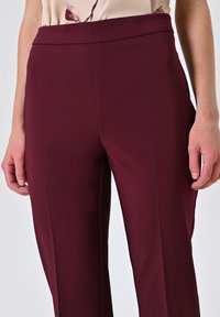 Bordeaux op maat gemaakte broek met een gladde textuur, hoge tailleband en zijnaadzakken, met een strakke, aansluitende silhouet.
