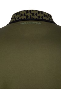 Olivově zelené polo tričko s černým a olivovým vzorovaným límcem, s vyraženým nápisem "KARL LAGERFELD" na zádech. Hladká textura.