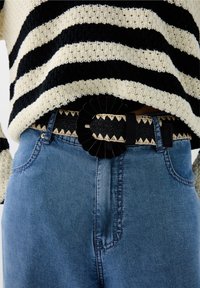 Pull en tricot rayé noir et crème associé à un jean en denim bleu. Une large ceinture avec une boucle texturée noire et un motif tissé décoratif.