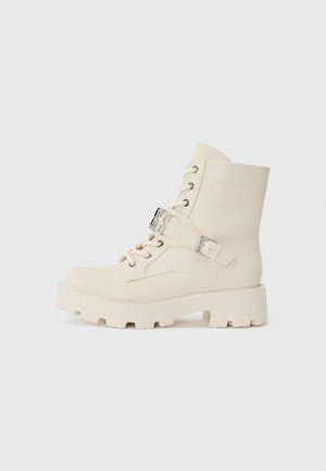 Krämfärgade ankelboots med en blandning av slät läder och texturerad kanvas. Kraftig gummisula med snörning framtill och justerbar remdetalj.