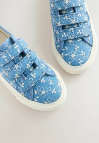 Baskets en toile bleue avec broderie florale blanche, dotées de deux bandes Velcro, bout rond et semelle en caoutchouc blanche.