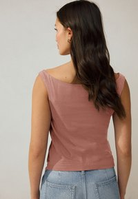 Top roz cu croială mulată, cu decolteu larg pe umeri și textură netedă, combinat cu blugi bleu deschis, cu talie înaltă și buzunare pe spate.