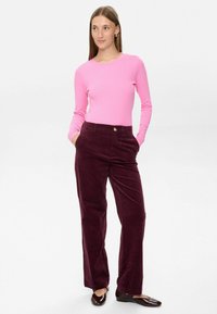 En figurnära rosa långärmad topp som är ihop med raka mörk vinröda kordbyxor, som har sidofickor och knappstängning. Skimrande bruna ballerinaskor.