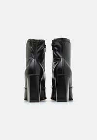 Botas de tobillo de cuero negro con tacón cuadrado, cierre de cremallera y costuras decorativas a lo largo de las costuras. Textura suave, diseño moderno.