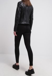 Chaqueta de cuero negro con un diseño ajustado y costuras visibles, combinada con jeans skinny negros y zapatos negros con cordones.