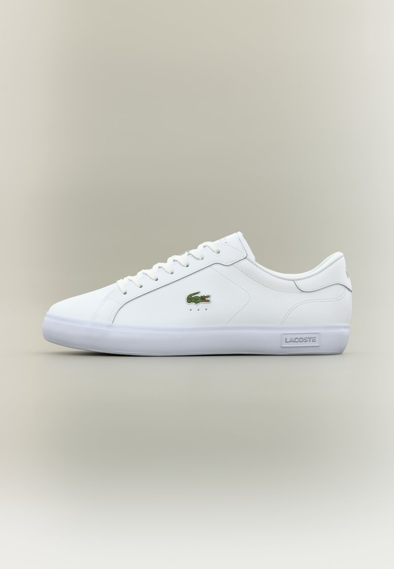 Baskets Lacoste blanches basses avec logo crocodile vert sur le côté et marquage Lacoste sur la semelle blanche, photographiées sur un fond neutre.