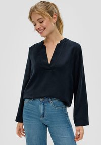 Marineblauw blouse met lange mouwen en V-hals, gemaakt van een gladde stof. Heeft een relaxte pasvorm en subtiele stiksels. G gecombineerd met blauwe jeans.